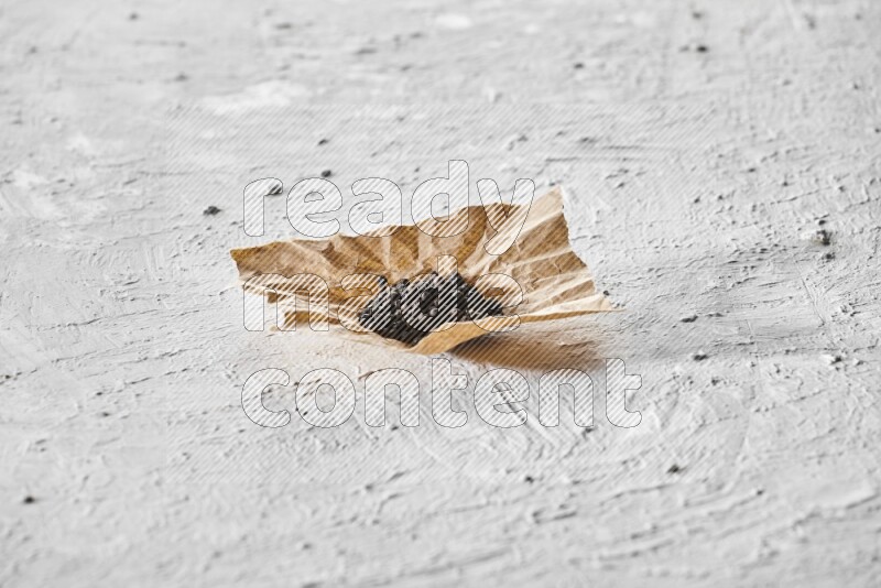 Black pepper on a crumpled paper on a textured white flooring