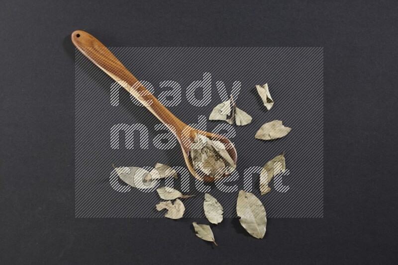 A wooden ladle filled with dried bay leaves on black flooring