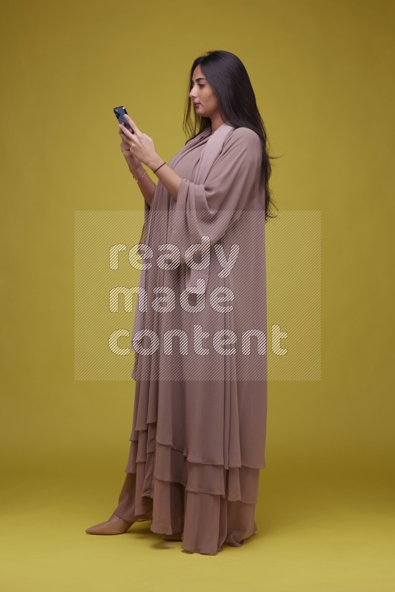 A woman Texting on a Yellow Background wearing Brown Abaya