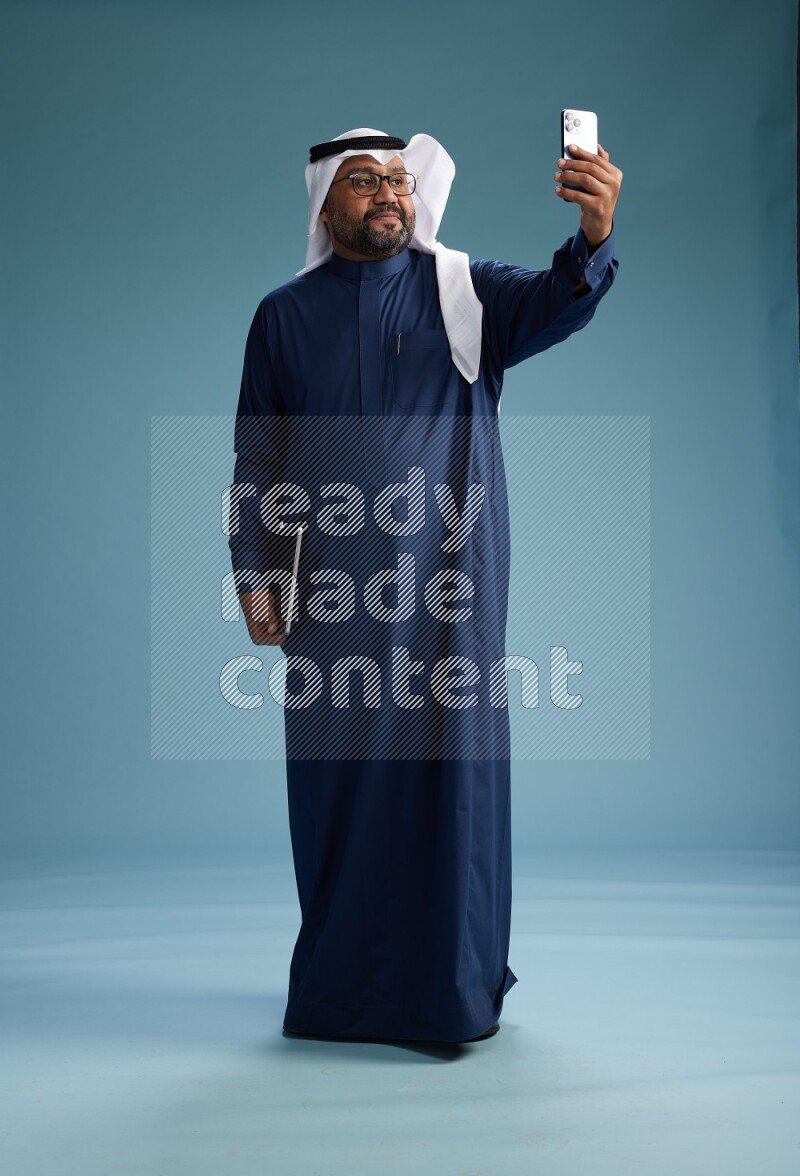 Saudi Man with shimag Standing taking selfie on blue background