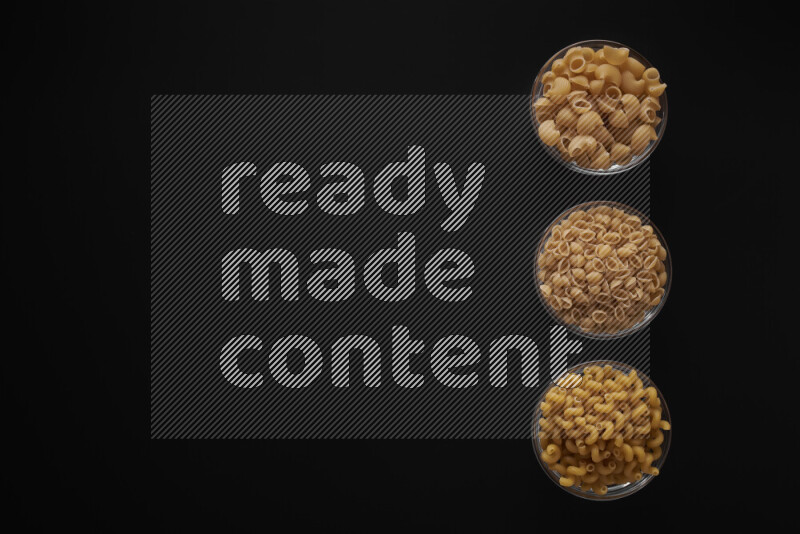 Different pasta types in 3 glass bowls on black background