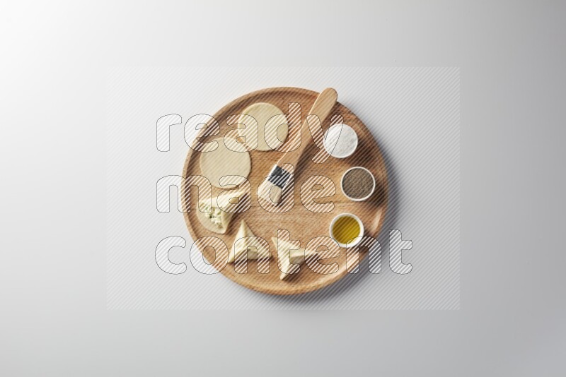 two closed sambosas and one open sambosa filled with cheese while salt, black pepper and oil with oil brush aside in a wooden dish on a white background