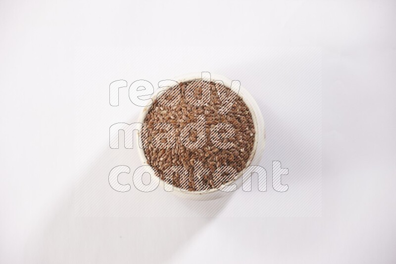 A pottery beige bowl full of flax seeds on a white flooring