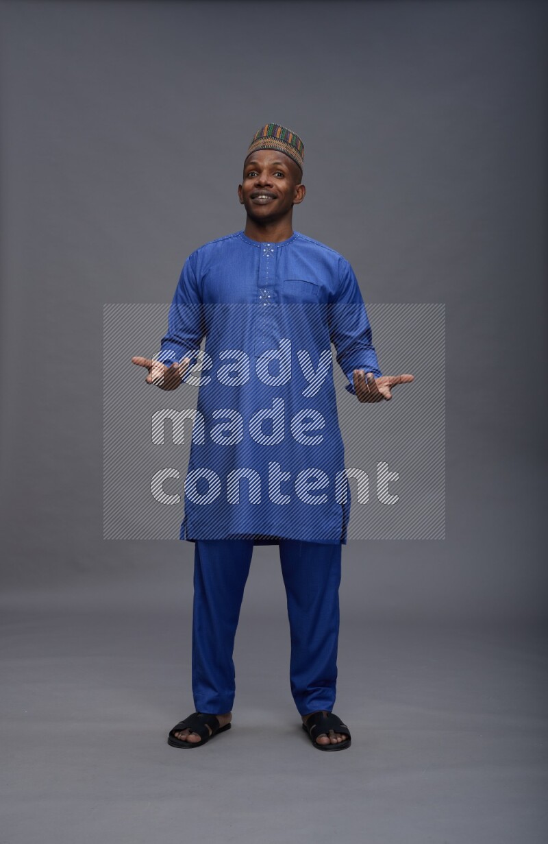 Man wearing Nigerian outfit standing interacting with the camera on gray background