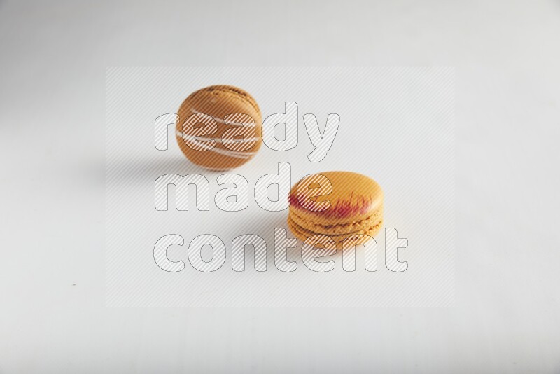 45º Shot of of two assorted Brown Irish Cream, and Orange Exotic macarons on white background