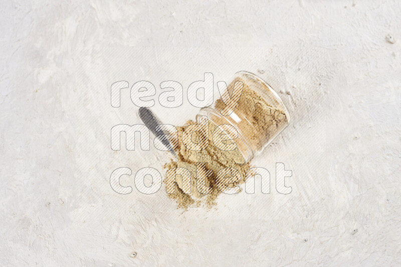 A glass jar full of ground ginger powder flipped with some spilling powder on white background