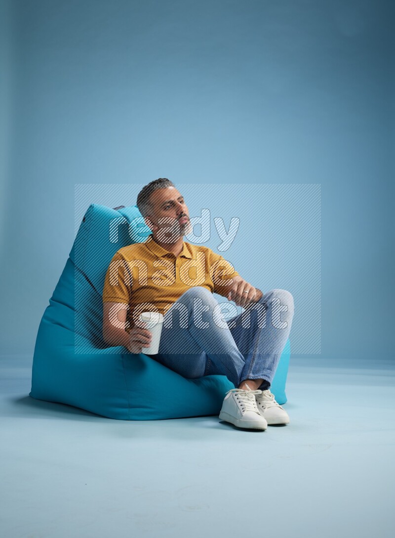 A man sitting on a blue beanbag and drinking coffee