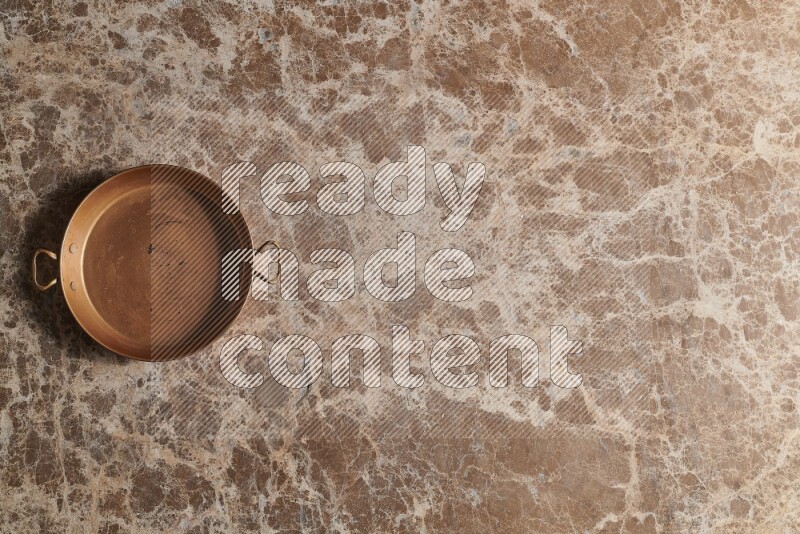 A small copper pan on beige marble background
