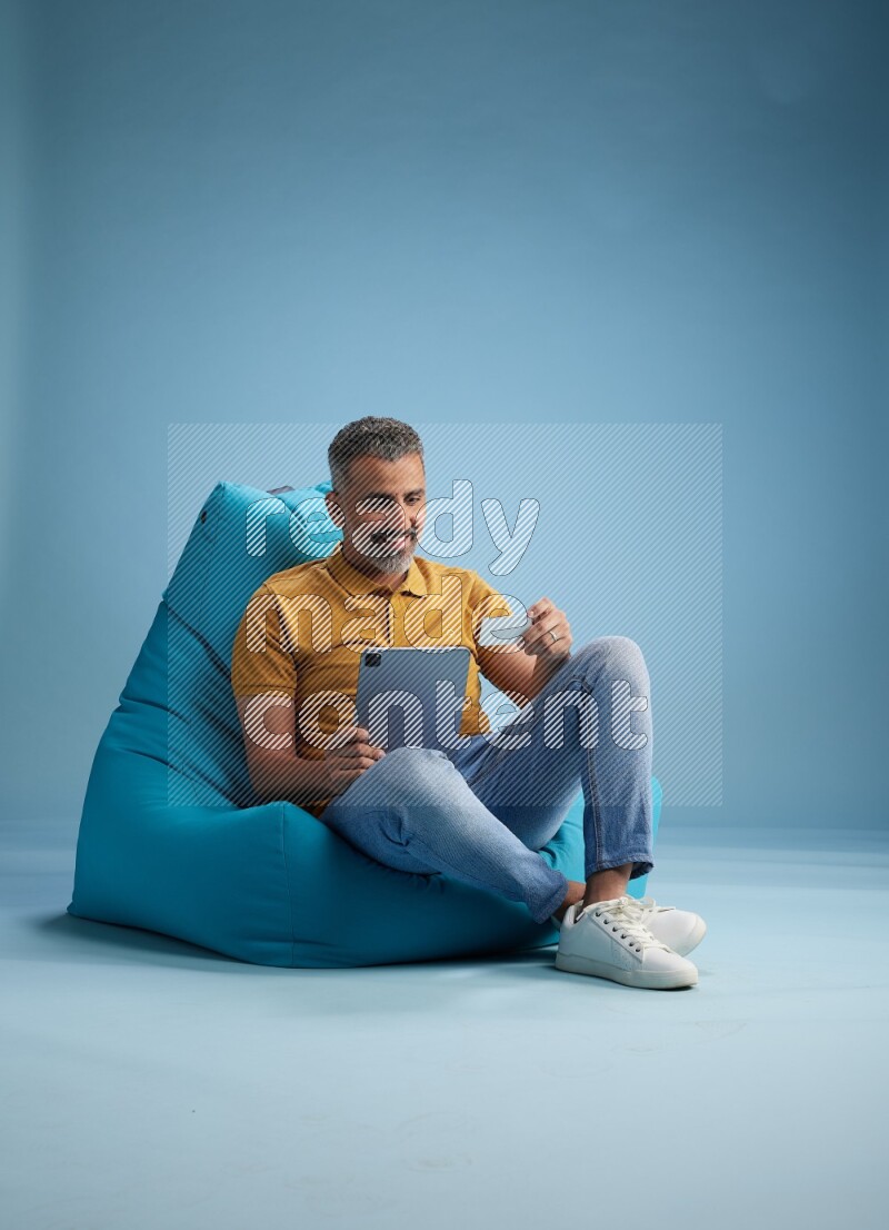 A man sitting on a blue beanbag and holding ATM card with tablet