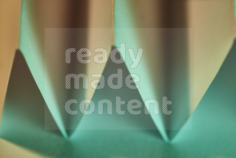 A close-up abstract image showing sharp geometric paper folds in green gradients and warm tones