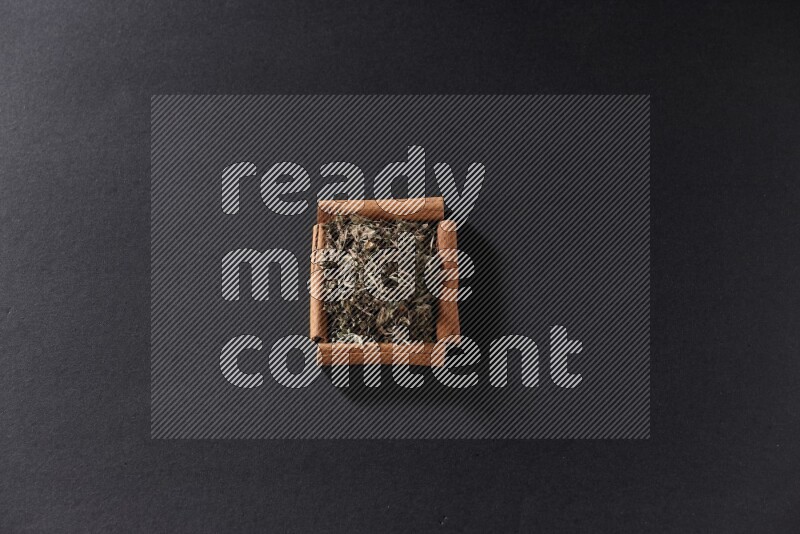 A single square of cinnamon sticks full of dried basil on black flooring