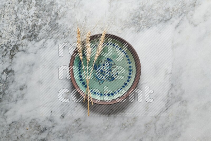 Wheat stalks on decorative pottery plate on grey marble background
