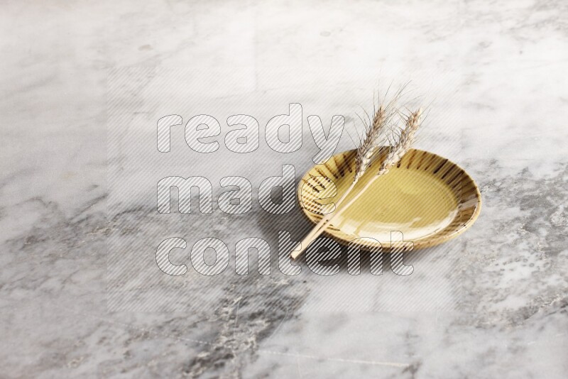 Wheat stalks on multicolored pottery plate on grey marble background