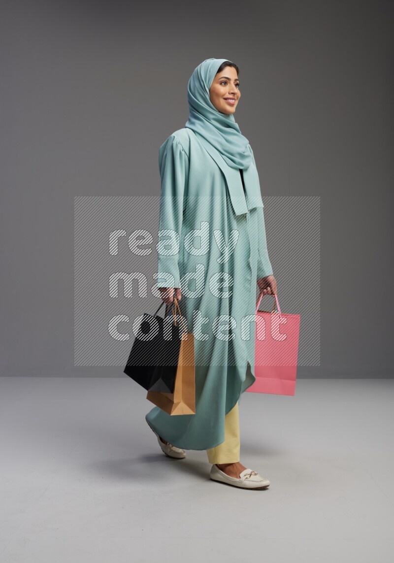 Saudi Woman wearing Abaya standing holding shopping bag on Gray background