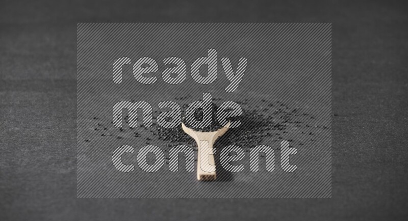 A wooden spoon full of black seeds and surrounded by seeds on a black flooring