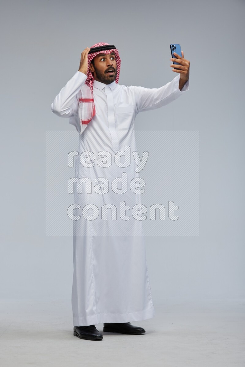 Saudi man Wearing Thob and shomag standing taking selfie on Gray background