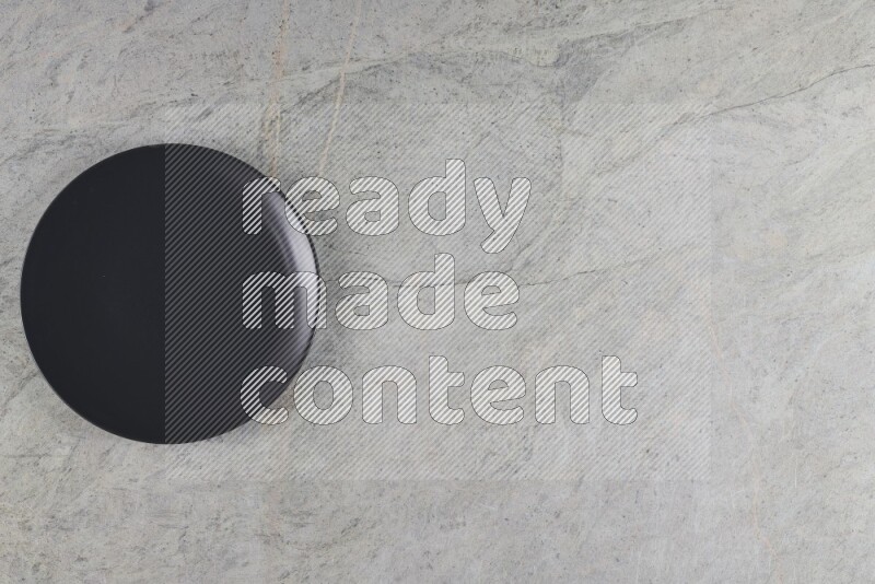A black ceramic circular plate on grey marble background