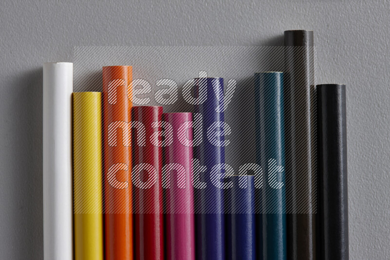 A collection of colored pencils arranged showcasing a gradient of different hues on grey background