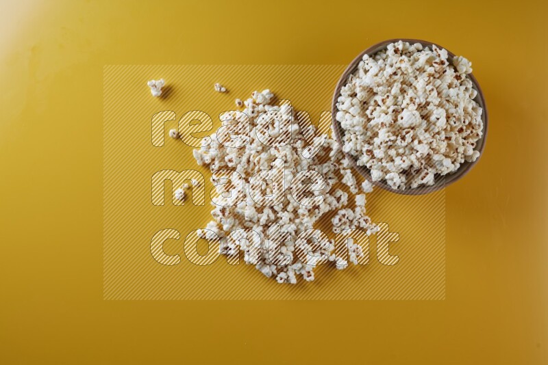 A brown pottery bowl full of popcorn with popcorn beside it on a yellow background in different angles