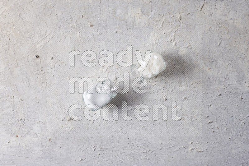 2 glass jars one is filled with table salt and the other with coarse sea salt on white background