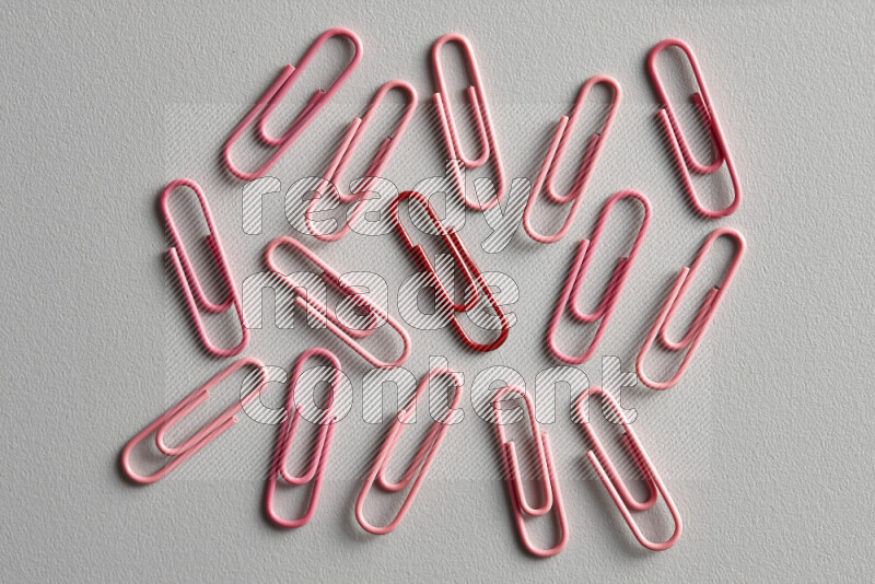 A bunch of pink paper clips with a different colored paper clip in the center on grey background