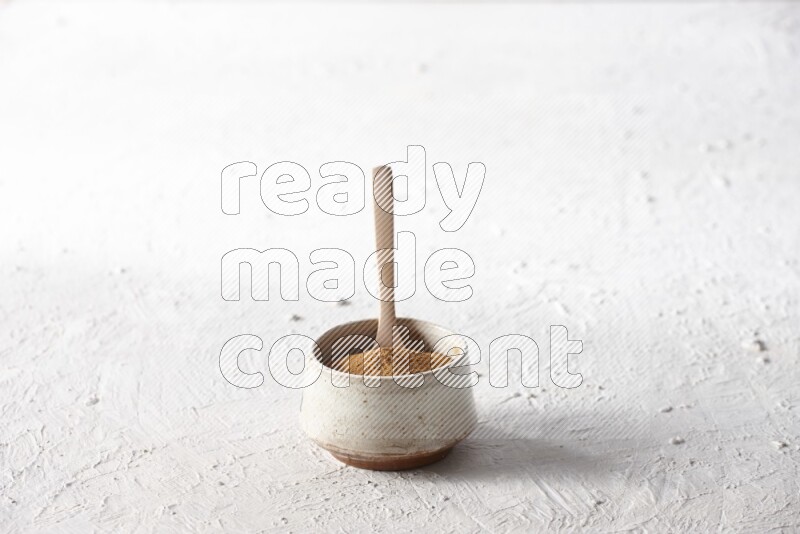 Ceramic beige bowl full of cinnamon powder with a wooden spoon on a textured white background