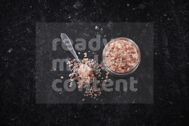 A glass jar full of coarse himalayan salt crystals on black background