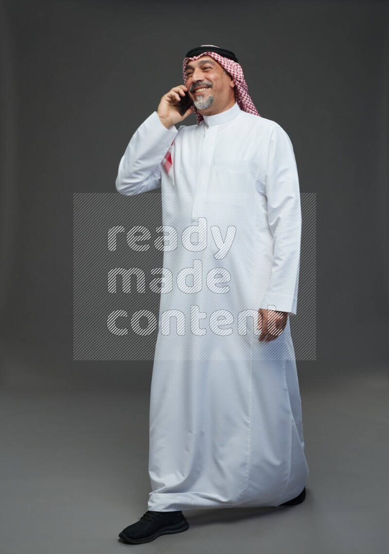 Saudi man with shomag Standing talking on phone on gray background