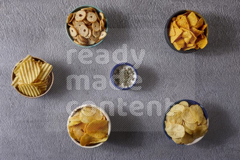 Assorted snacks in pottery bowls on grey background