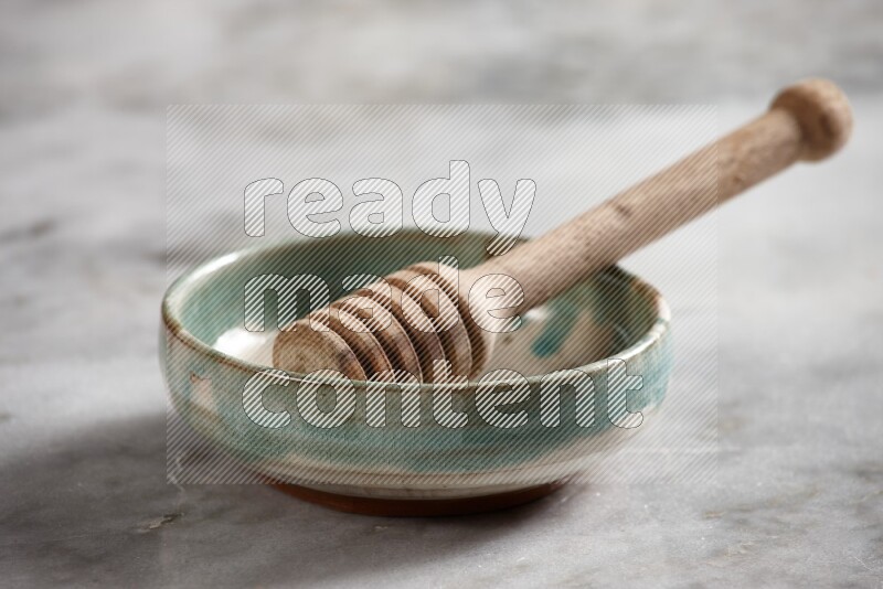 Multicolored pottery bowl with wooden honey dipper in it on grey marble background