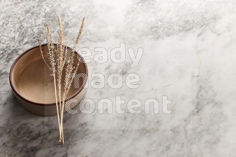 Wheat stalks on beige pottery oven bowl on grey marble background
