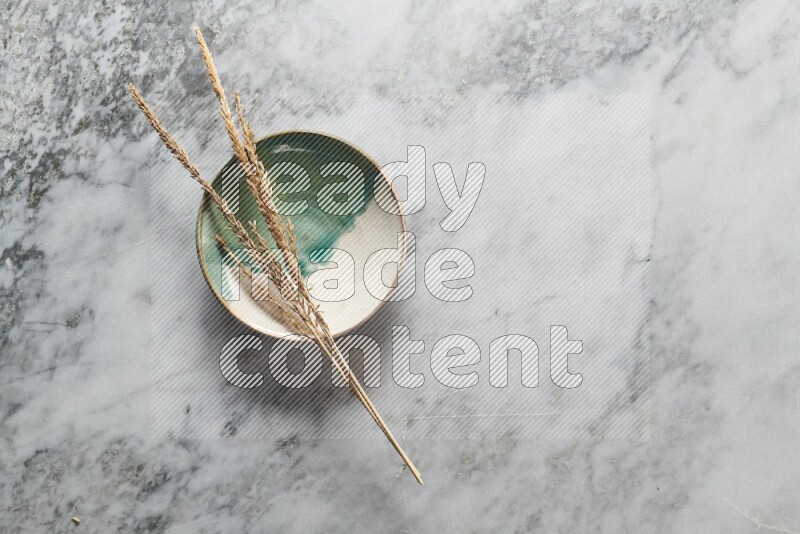 Wheat stalks on multicolored pottery plate on grey marble background
