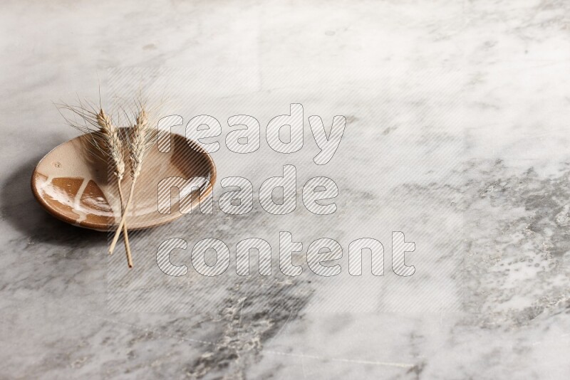 Wheat stalks on multicolored pottery plate on grey marble background