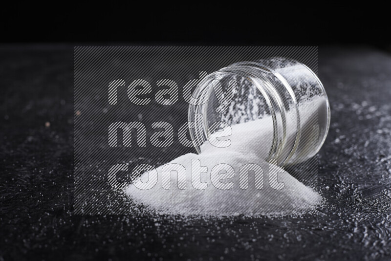 A glass jar full of fine table salt on black background