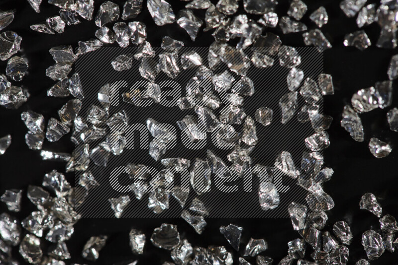 Silver shimmering fragments of glass scattered on a black background