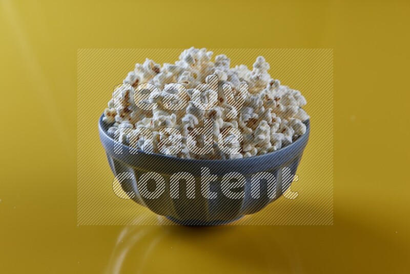 A blue pottery bowl full of popcorn on a yellow background in different angles