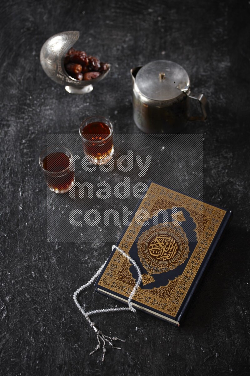 Moshaf with tea cups and prayer beads in a dark setup