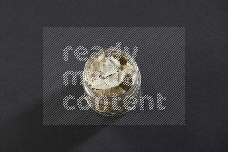 A glass jar filled with dried bay leaves on black flooring