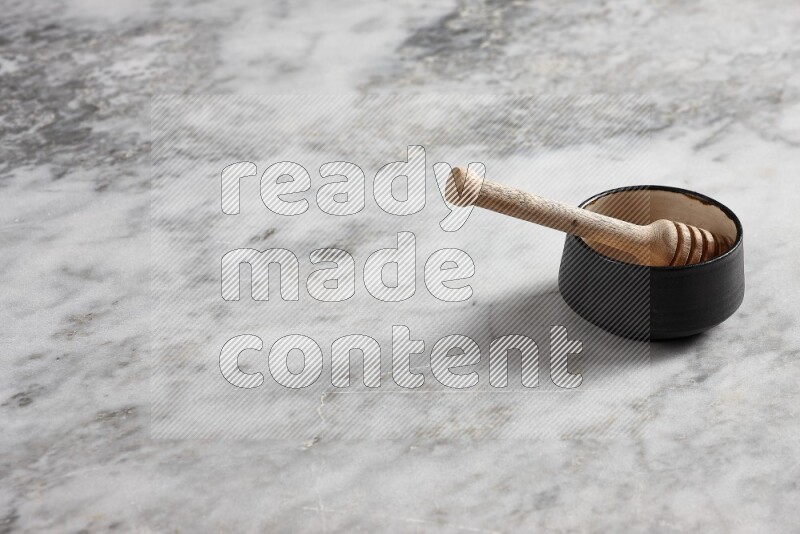 Black pottery bowl with wooden honey dipper in it on grey marble background