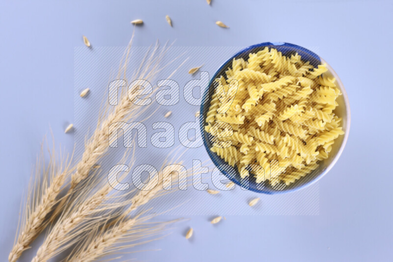 Raw pasta with wheat stalks on light blue background