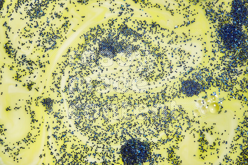 A close-up of sparkling blue glitter scattered on swirling yellow background