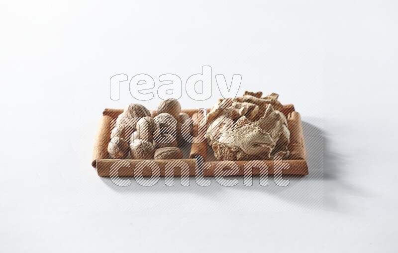 2 squares of cinnamon sticks full of dried ginger and nutmegs on white flooring