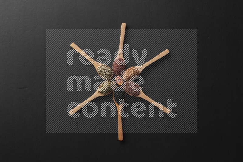 wooden spoons filled with white peppers, mustard seeds, black seeds, garden cress, cumin and flax on black flooring and shaped like a clock