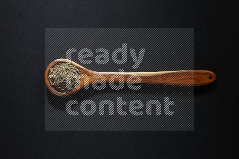 A wooden ladle full of cumin seeds on black flooring