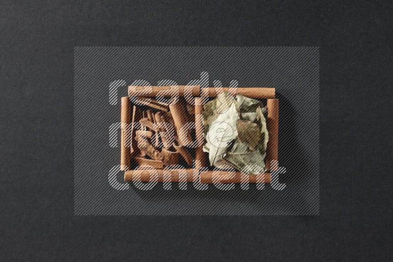 مربعان من أعواد القرفة ممتلئان بقطع من القرفة وأوراق الغار علي خلفية سوداء