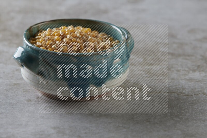 corn kernel in a multi-colored handheld ceramic bowl on a grey textured countertop