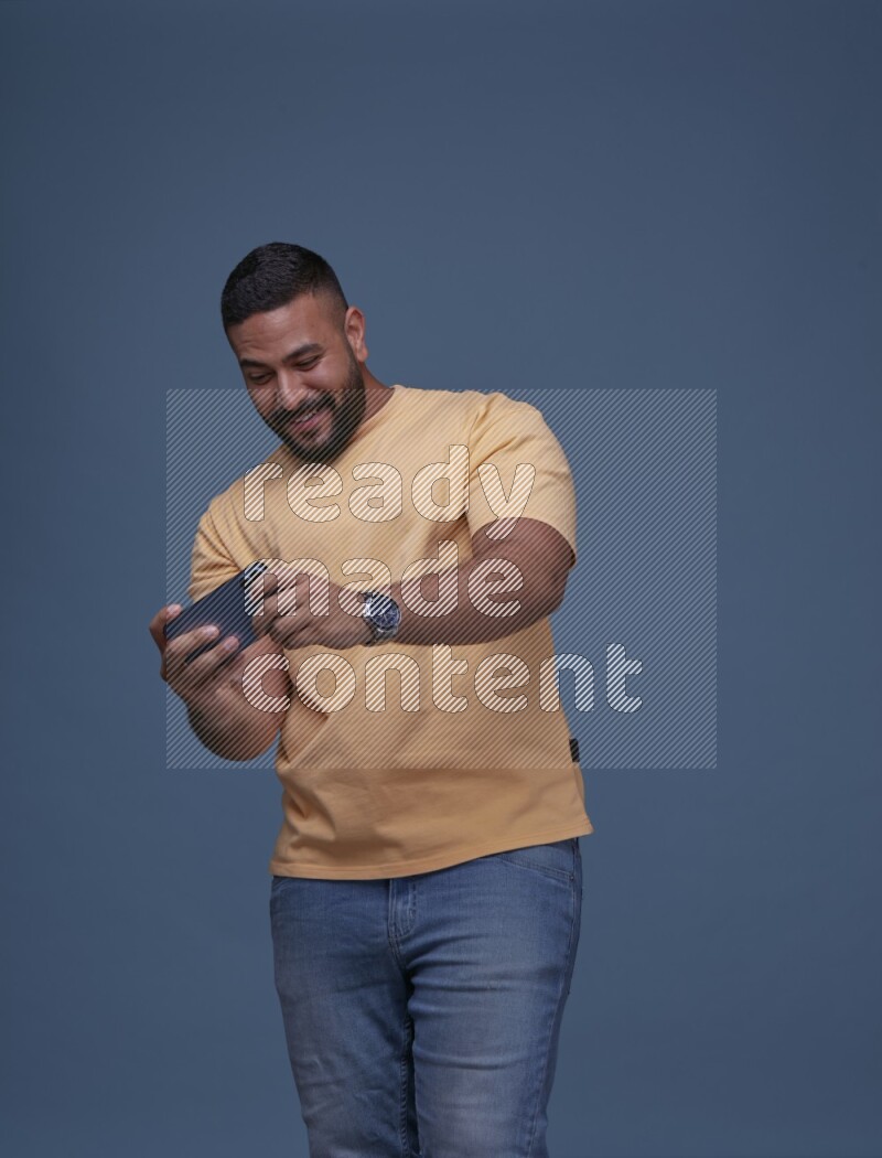 A man Playing Games on Smartphone on Blue Background wearing Orange T-shirt