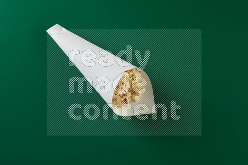 A paper cone full of popcorn on a green background in a top veiw shot