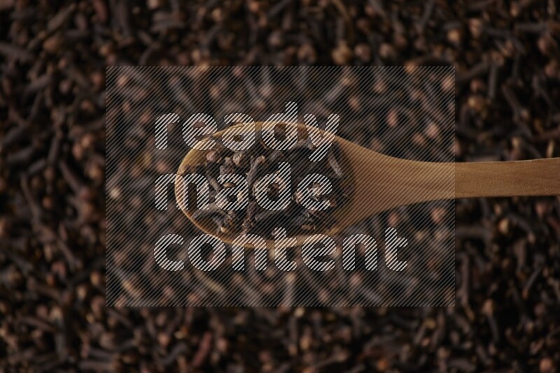 A wooden spoon full of cloves on cloves background and black flooring
