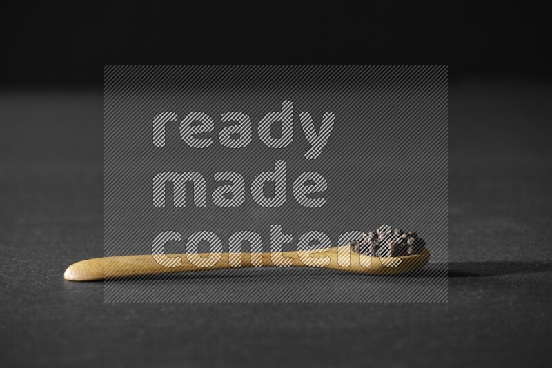A wooden spoon full of black pepper on a black flooring